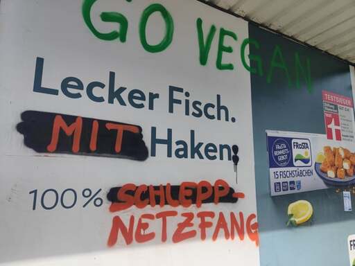 Fischstäbchen Werbeplakat von Frosta. Der Slogan "Lecker Fisch. Ohne Haken. 100% frei von Zusätzen." wurde teilweise mit Graffiti überschrieben zu: "Lecker Fisch. Mit Haken: 100% Schleppnetzfang."

Darüber in grüner Schrift: "Go vegan"