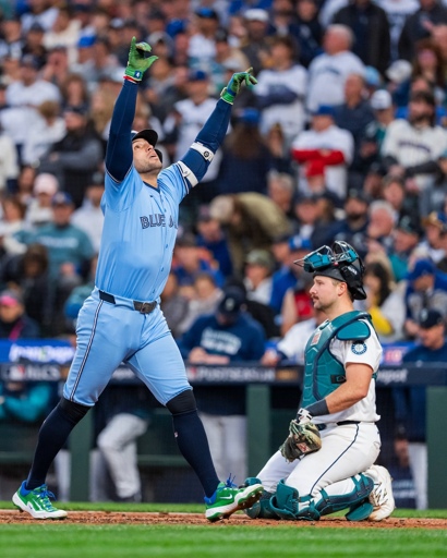 Pic of George Springer from ALCS game 3 right after a successful at bat, probably a home run. George's hands are stretched upwards and he's looking towards the sky. Cal "Big Dumper" Raleigh squats behind homeplate in the background looking a little concerned